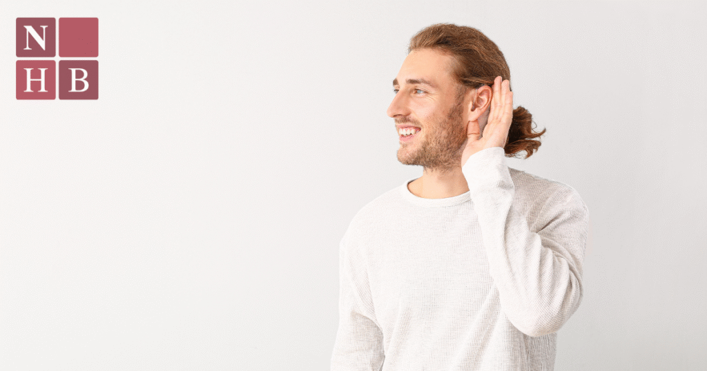 Smiling man cupping his ear to hear better, representing hearing loss symptoms and Eustachian Tube Dysfunction diagnosis at National Hearing & Balance.
